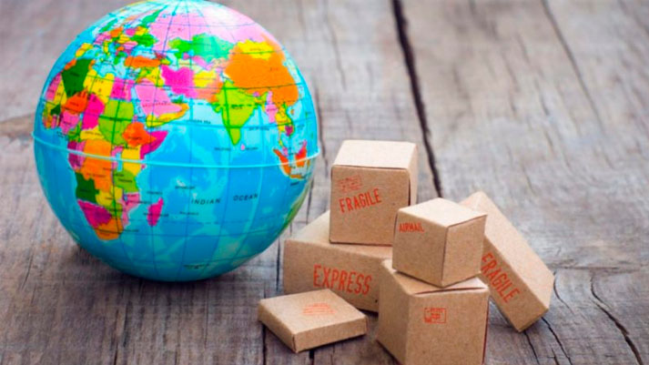 A imagem apresenta um globo terrestre colorido ao lado de pequenas caixas marcadas com as palavras "Fragile" e "Express", simbolizando o alcance global e as operações de comércio internacional típicas de 'Empresas Multinacionais'.