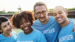 Quatro voluntários sorridentes com camisetas azuis onde se lê 'VOLUNTÁRIO' posando juntos para uma foto, destacada no tópico 'Marketing específico para entidades sem fins lucrativos' do post 'Entidades sem fins lucrativos'.