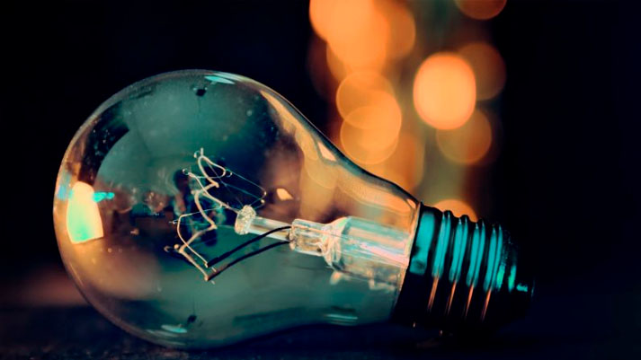 A imagem mostra uma lâmpada incandescente desligada contra um fundo escuro e desfocado com luzes alaranjadas, sugerindo a ideia de perda de brilho ou falha em iluminar o que pode ser uma alusão às '5 grandes empresas que morreram por falta de inovação'.