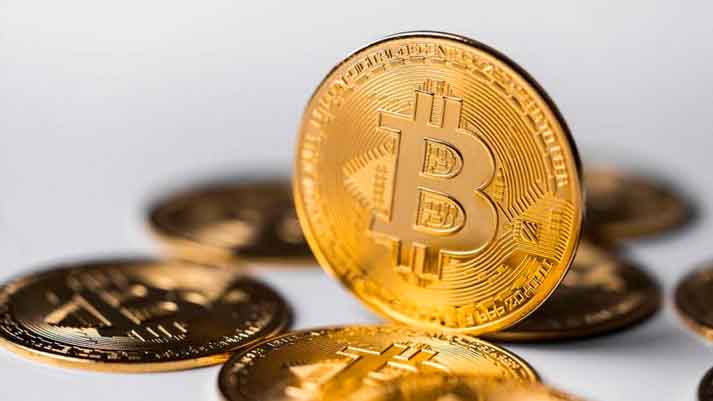 A imagem mostra várias moedas douradas com o símbolo do Bitcoin, sugerindo o tema de 'Criptomoeda', uma forma digital de dinheiro que utiliza criptografia para segurança nas transações.