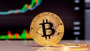 Uma representação física de uma moeda de Bitcoin está em primeiro plano com gráficos de mercado em ascensão ao fundo, simbolizando as "Vantagens da Criptomoeda" discutidas no post sobre 'Criptomoeda'.