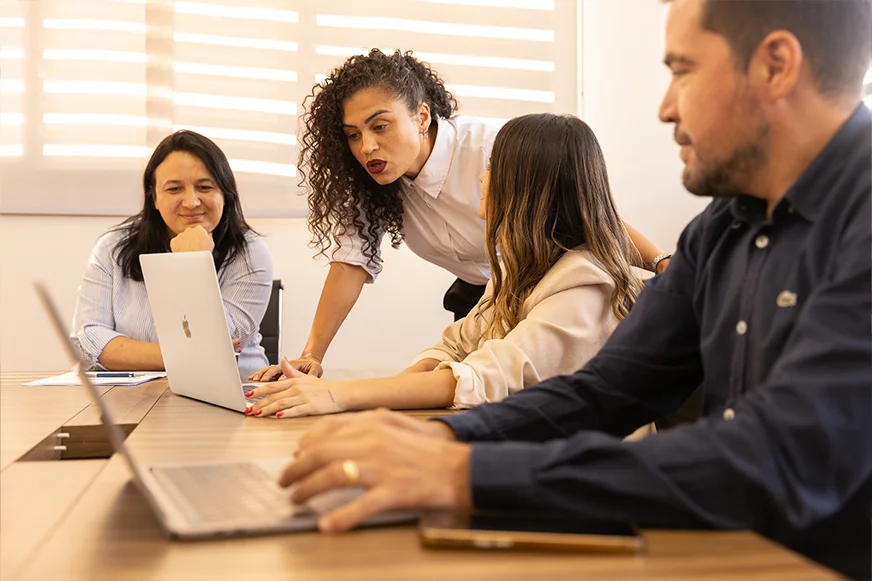 Quatro funcionários da OSP Contabilidade em uma discussão engajada ao redor de uma mesa com uma mulher em pé apontando para um laptop.